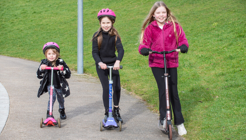 Three children riding scooters on-campus
