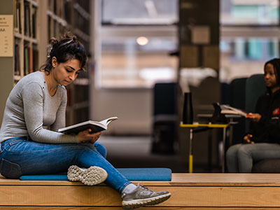 Student sitting on a wooden bench in the Library reading.