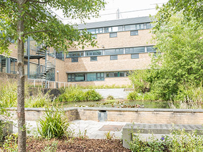 Lancaster Environment Centre, with trees and foliage present along with a pond and benches.