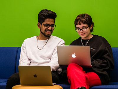 Two students are talking and smiling using laptops.