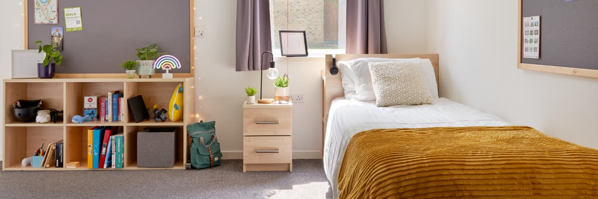An empty student bedroom has a bed on the right-hand side, and bookshelves on the left.
