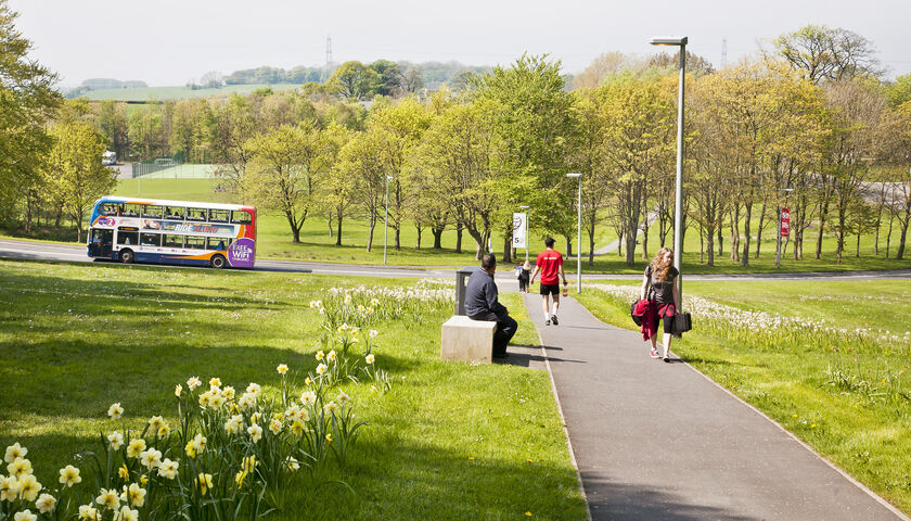 A bus driving through trees and daffodils up the University's driveway.