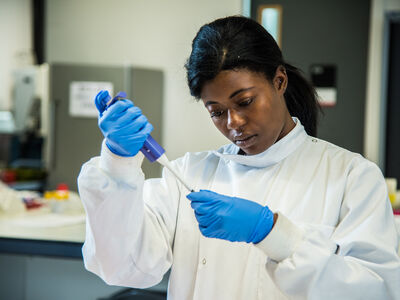 Student in a lab coat and blue gloves using a pipette