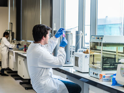 A student in a lab coat using equipment by a window in the biomedical lab