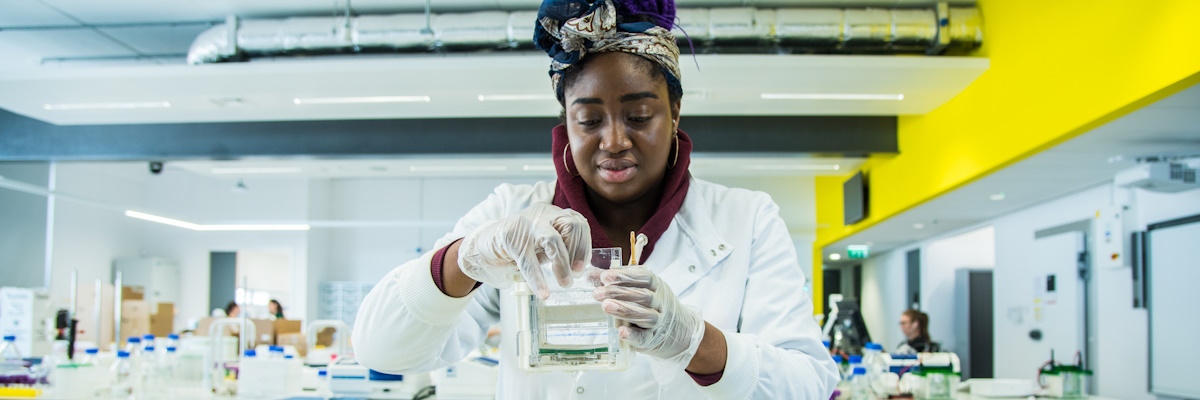 Student in a white lab coat at a laboratory bench, holding a sample