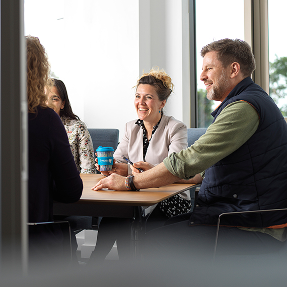 Four smiling people seated in an office meeting room
