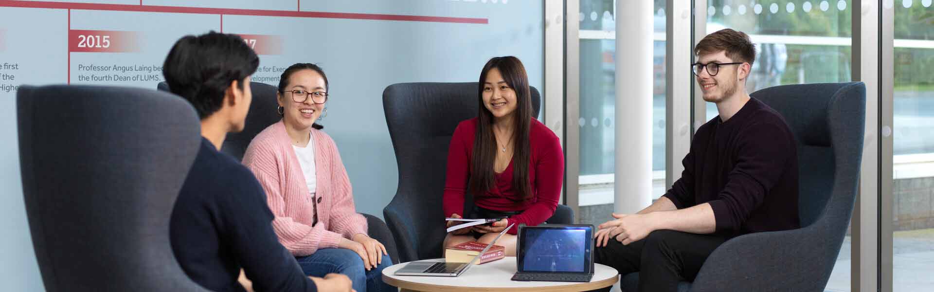 Four students seated around books and laptops on a coffee table, smiling