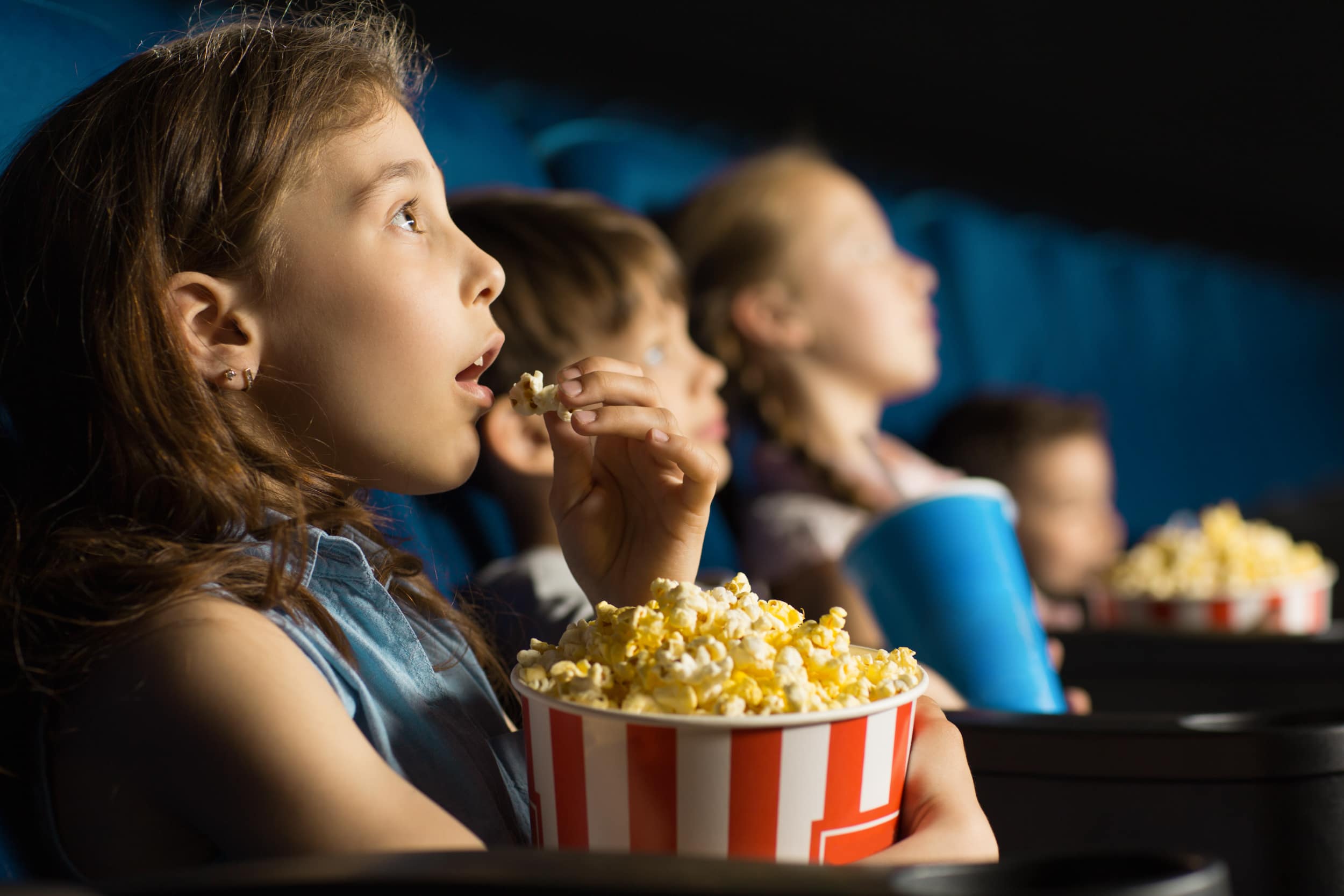 children sit in a cinema eating from a large tub of popcorm