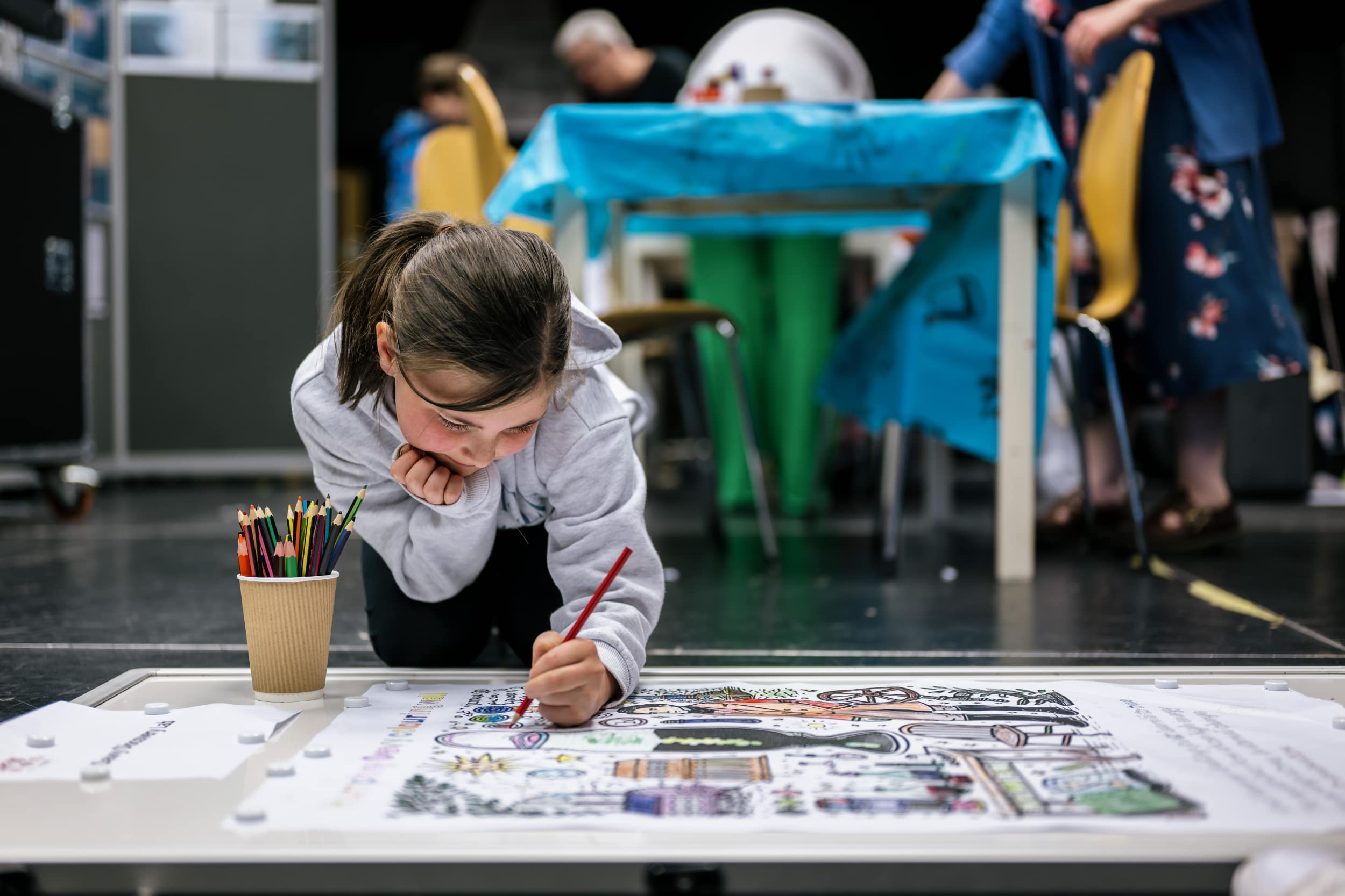 a young girl colours in a picture whilst kneeling on the floor