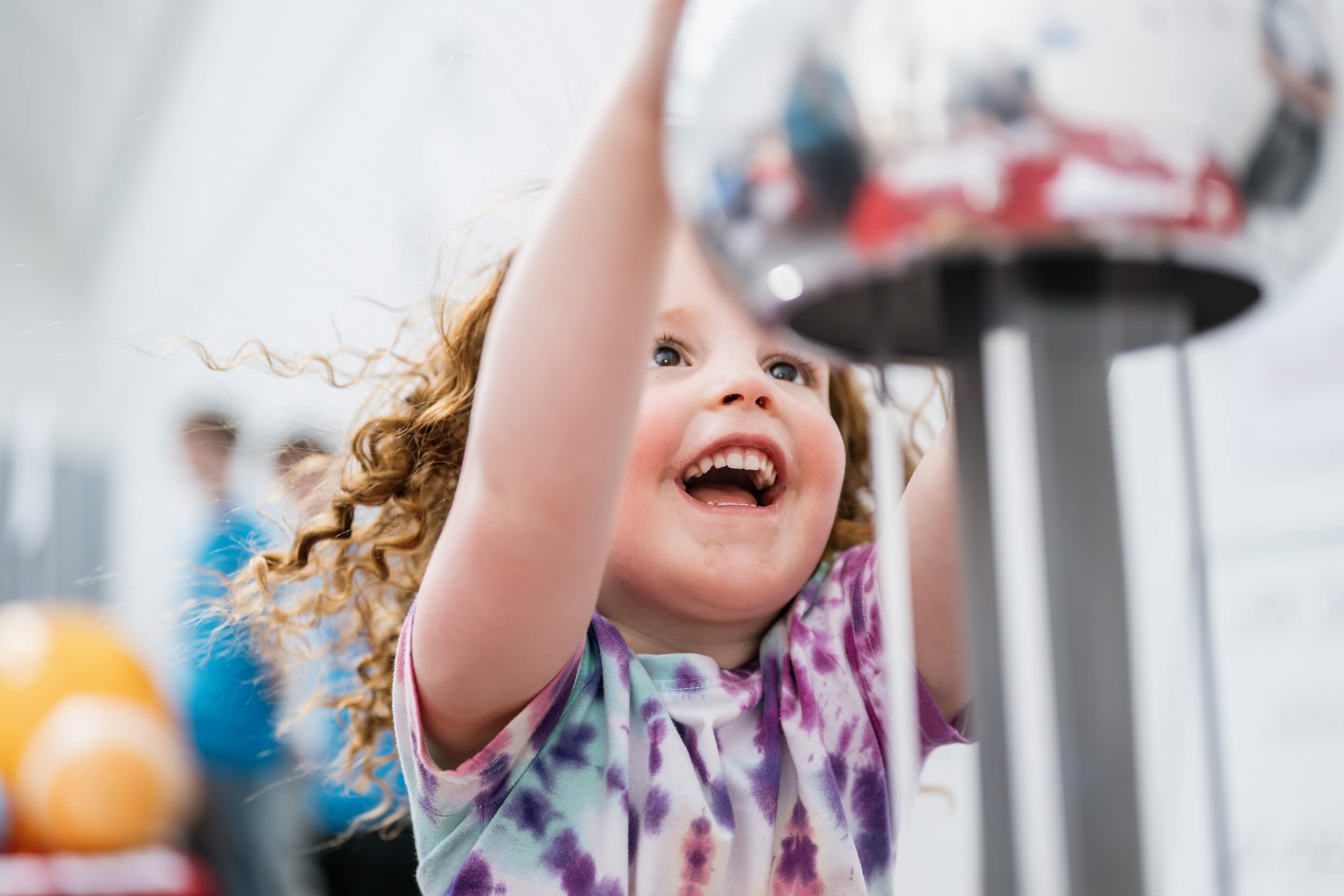 a young girl touches a large silver sphere which has made her hair stick up