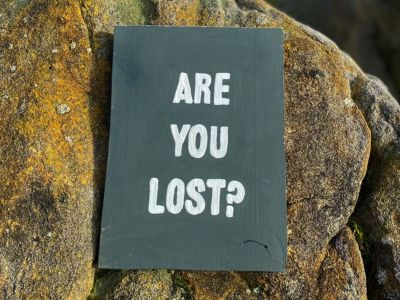 a slate sign saying are you lost is attached to a rock