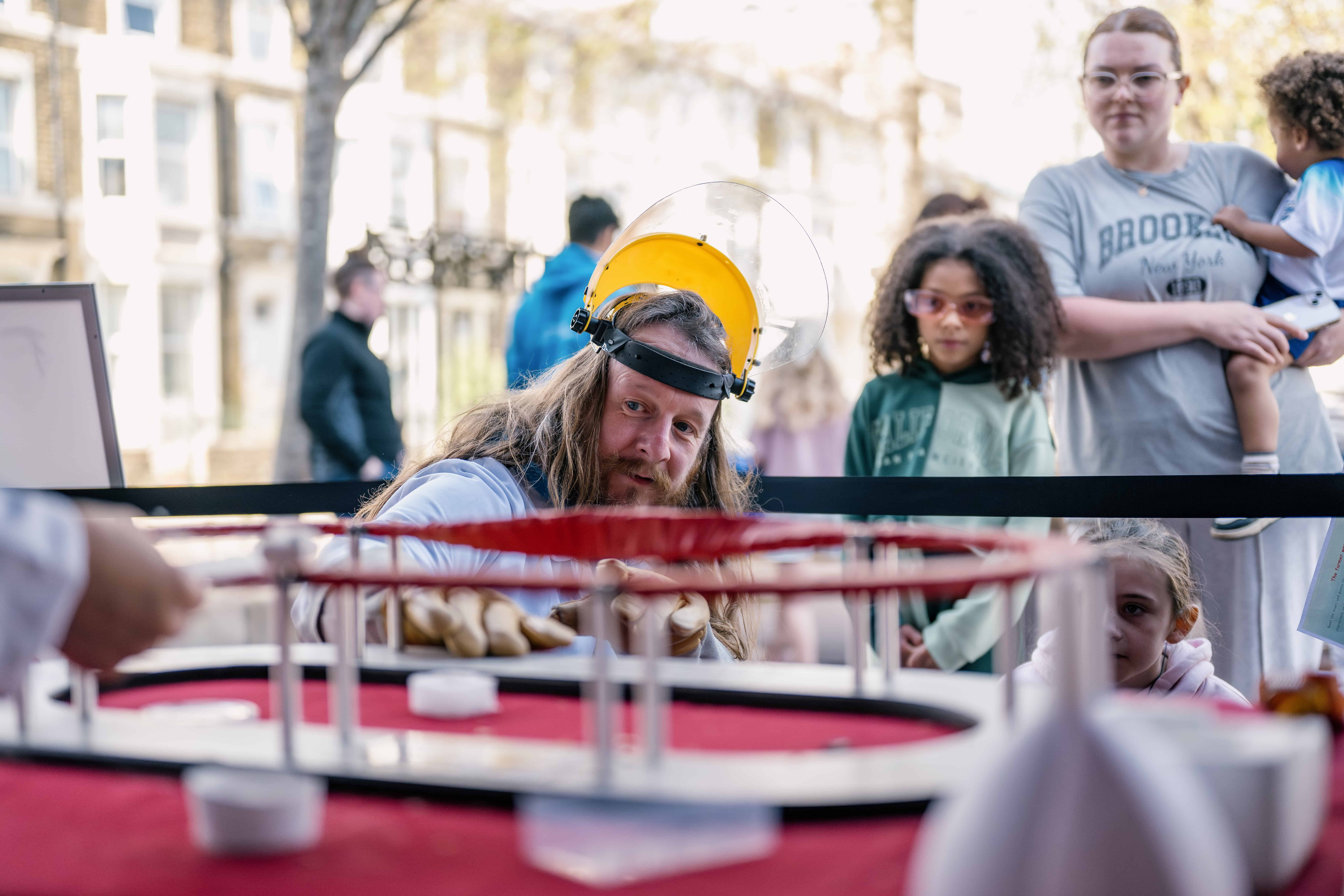 a family watch a man with long hear and a beard wears a protective visor on his head look at a test