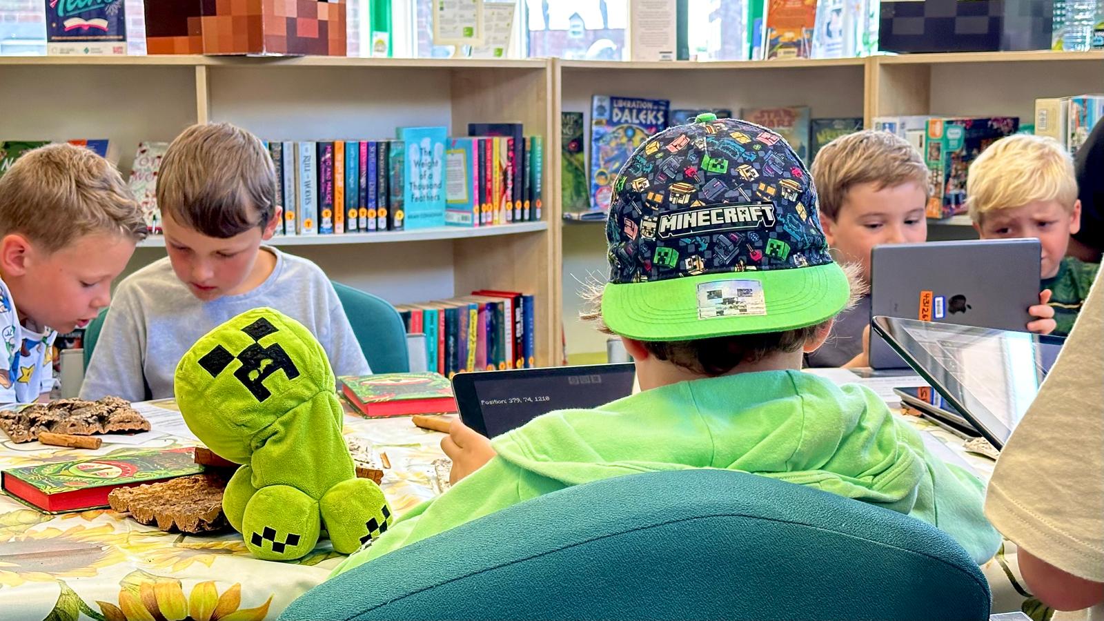 a group of children, one of whom wears a minecraft cap, play on ipads