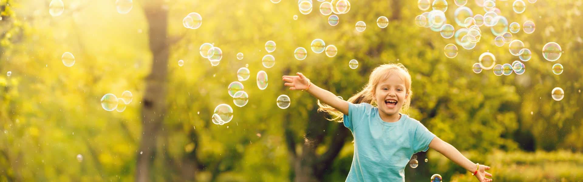 Little girl laughing in a field with soap bubbles