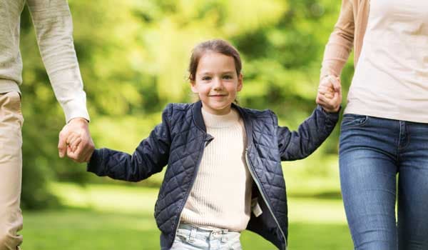  family walking in summer park girl holding hands with two adults