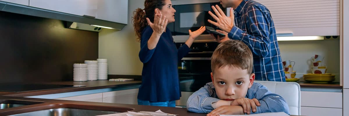 Sad boy looking at camera while his parents argue in the kitchen
