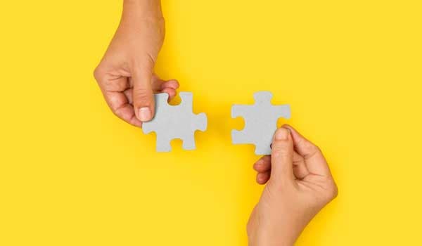 two hands trying to connect couple puzzle piece with yellow background