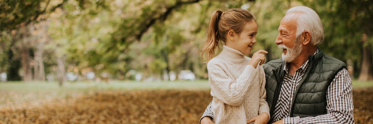 Grandfather spending time with his granddaughter in park on autumn day
