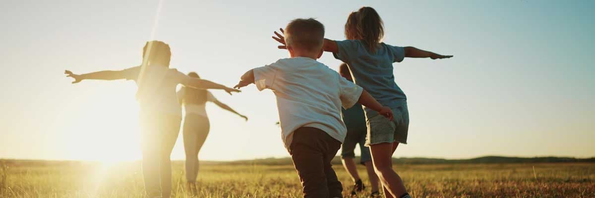 Group of children running in a sunny field with their arms outstretched