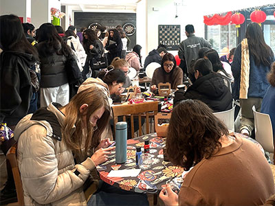 Tables filled with people sat crafting with other people standing by. 
