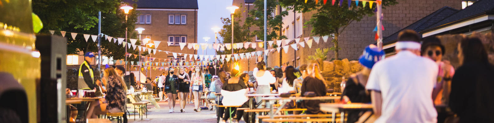students sitting at picnic benches with lights hung above them