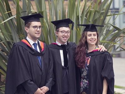 Three students dressed in their robes smiling at the camera