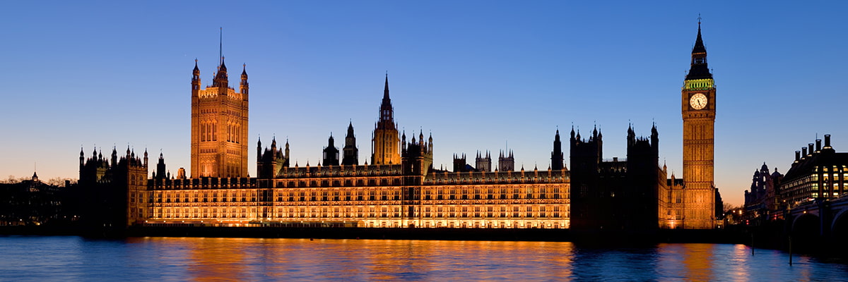 A view across the river Thames to the UK houses of parliament, lit up at dusk