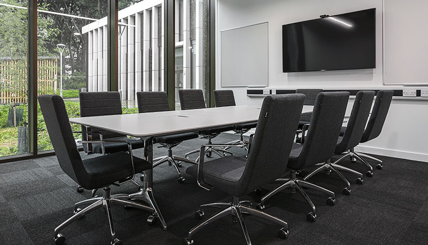 A meeting room in Health Innovation One with 9 chairs and a TV