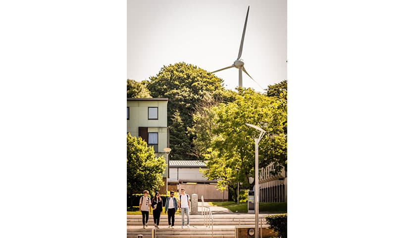 Students walking through campus with the university Wind turbine in the distance behind trees