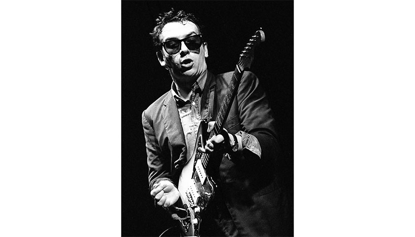 Elvis Costello performing with his guitar on the Great hall stage