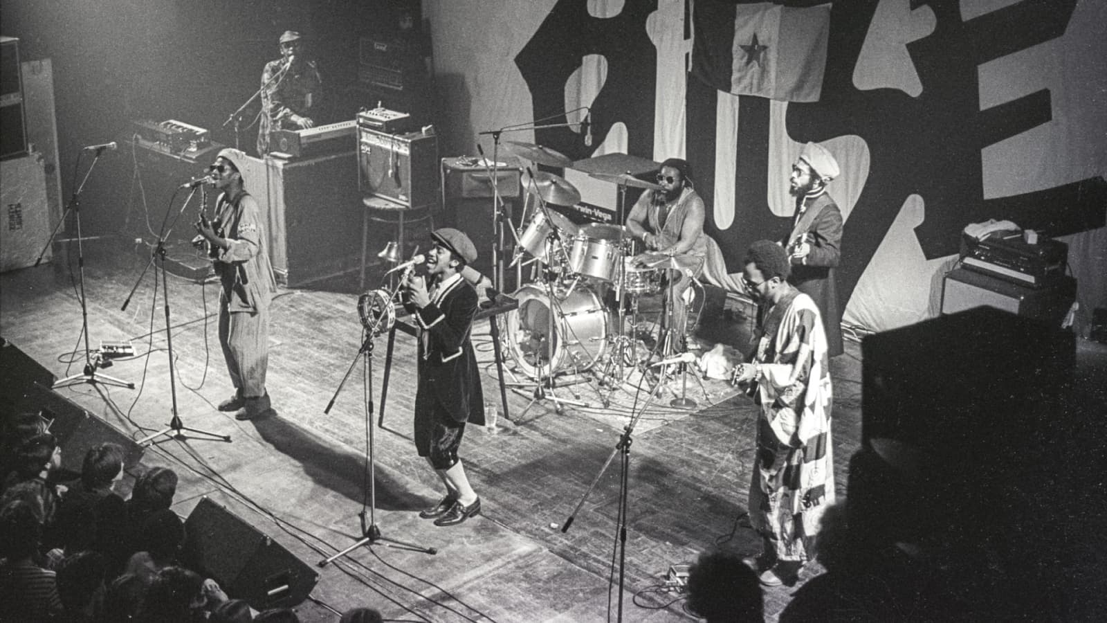 Reggae band Steel Pulse play on stage in front of a large banner with their name on.