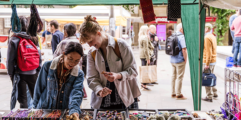 Two students looking at items at a market stall.