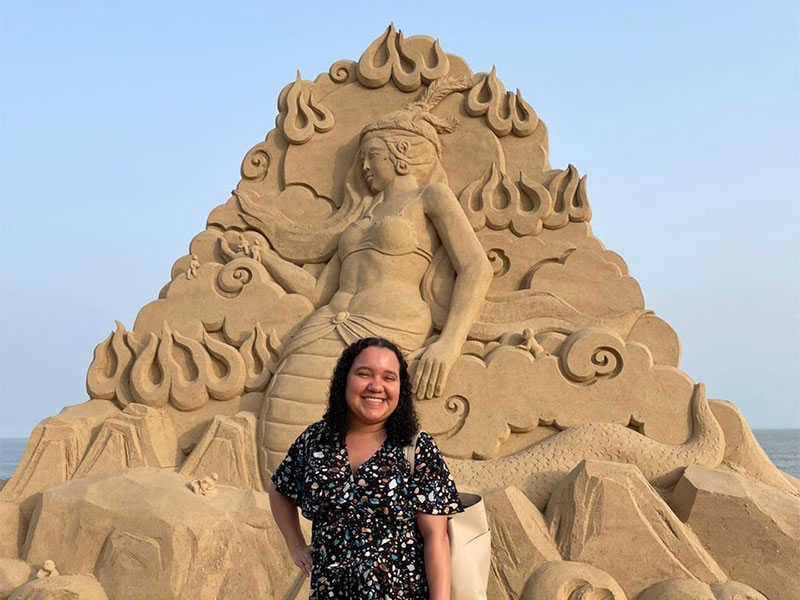 Lyea standing next to a sandcastle design.