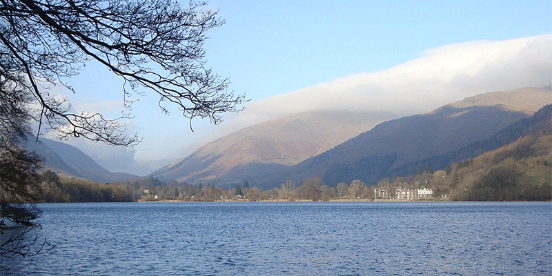 A view of a lake in Grasmere with mountains in the background on a sunny day.