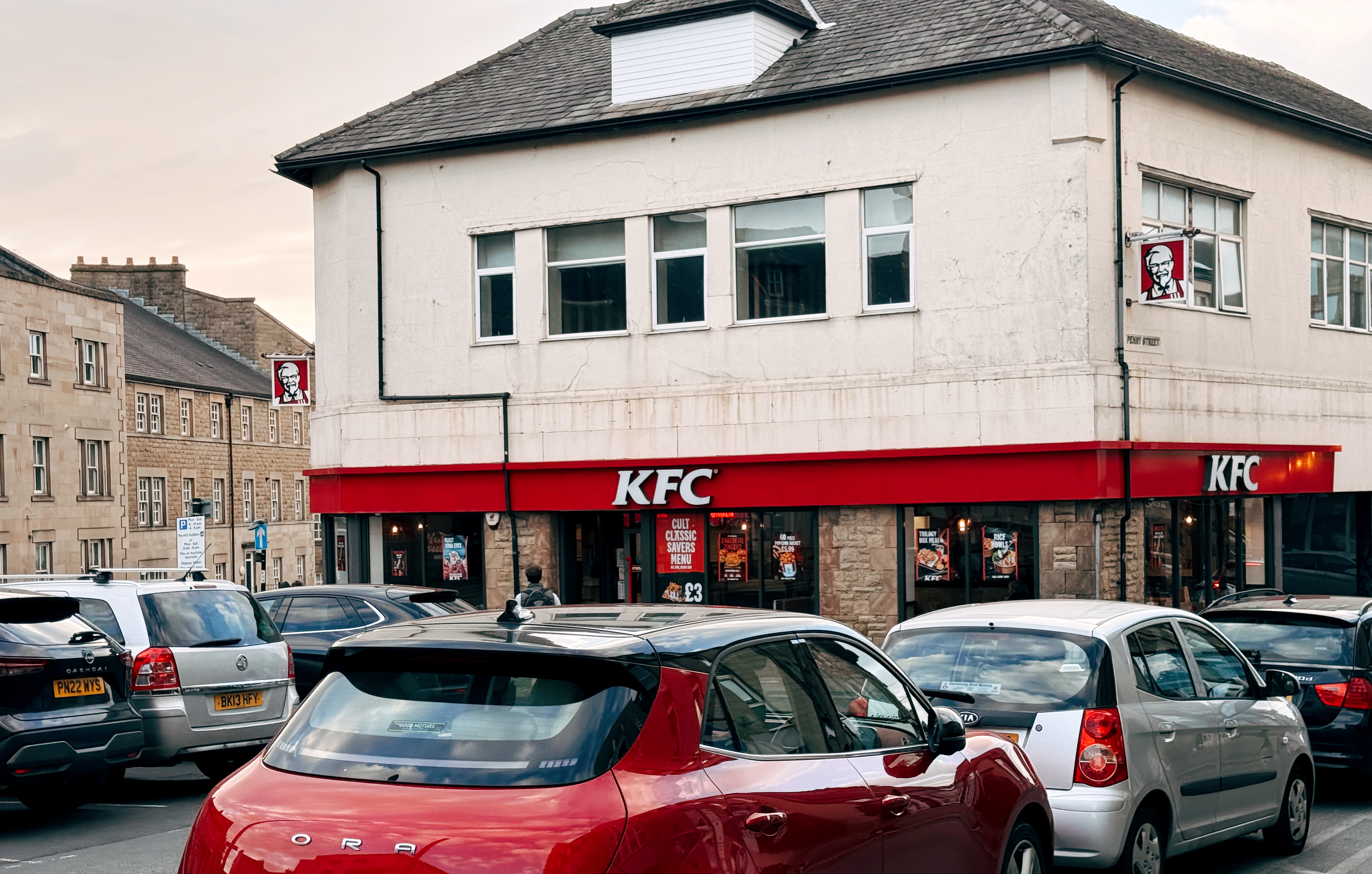 A KFC in Lancaster town centre with cars parking along the road.