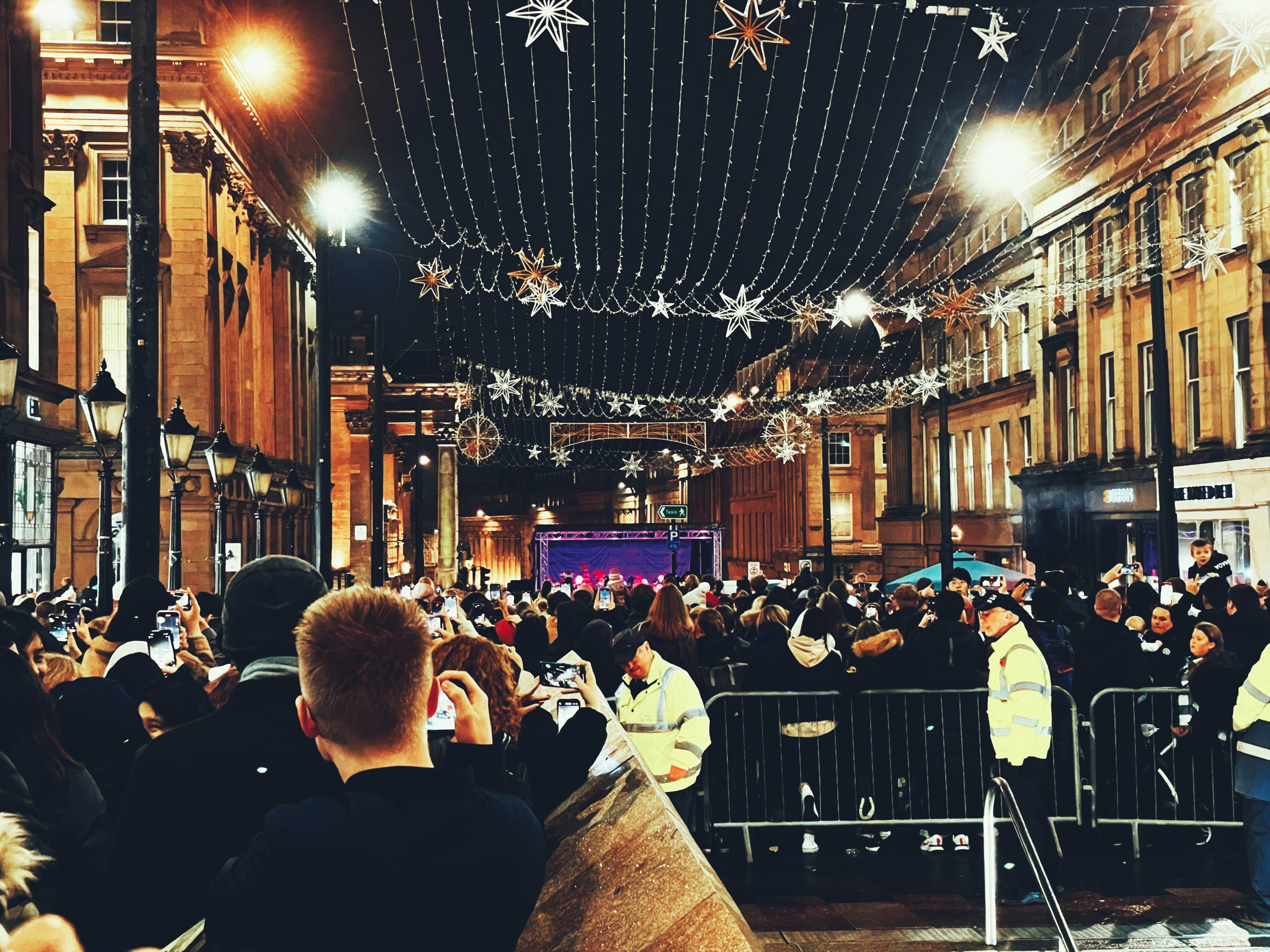 A crowd of people in town along the street watching a live performance. 
