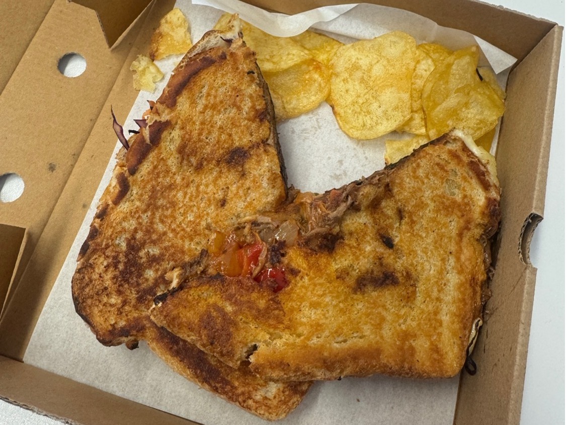 A beef brisket and cheese toastie with crisps on the side.