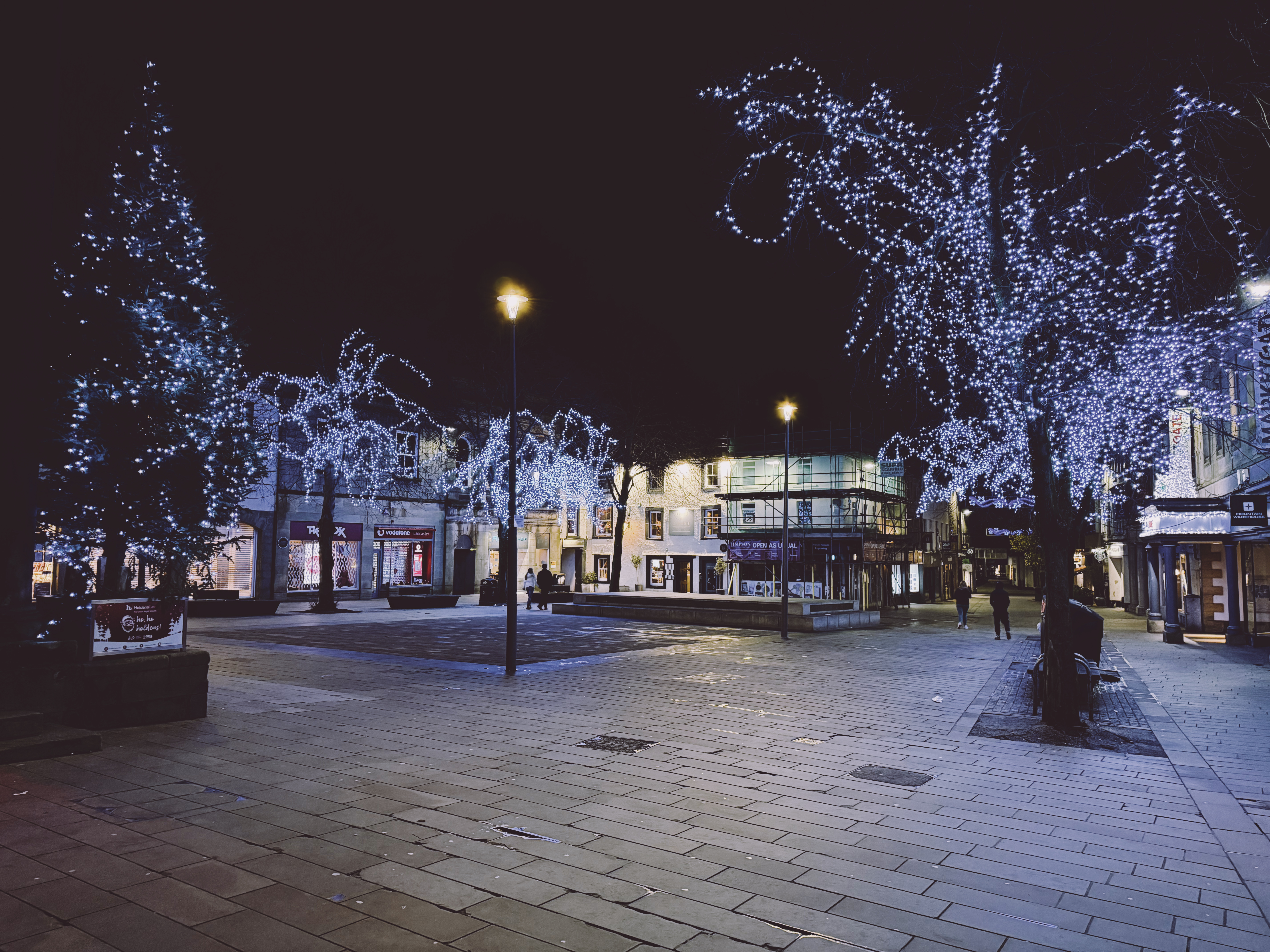 Lancaster town centre at night with shops and people around. 