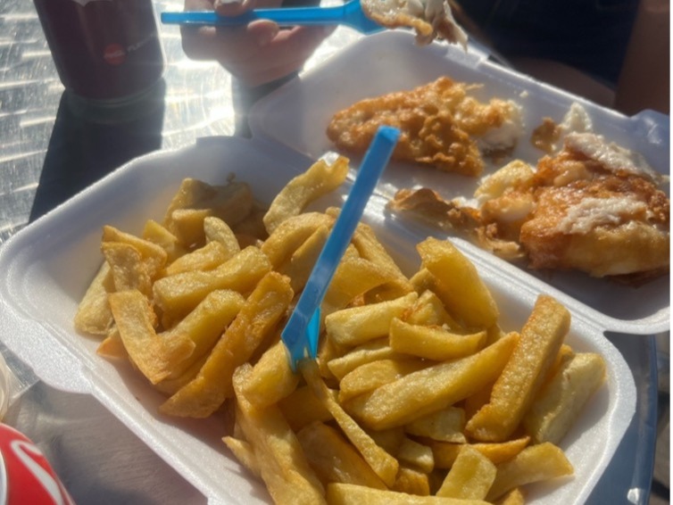 Two people sharing a fish and chips on a sunny day with cokes.