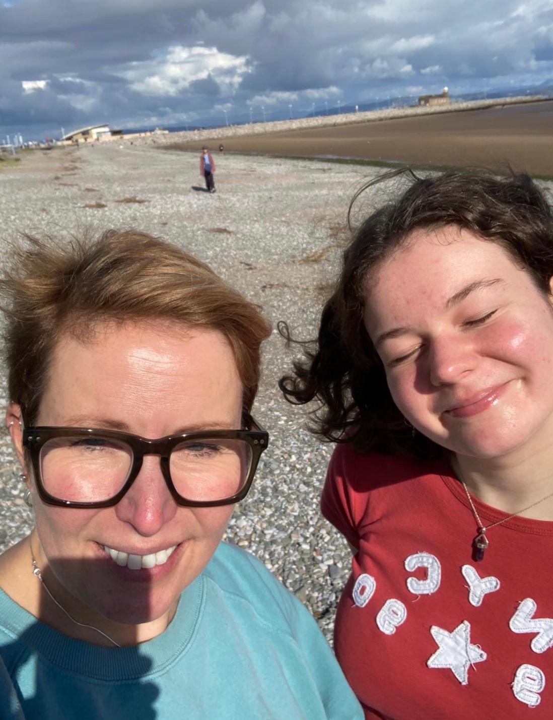 Martha and her mum smiling for a selfie near a seaside on a sunny day.