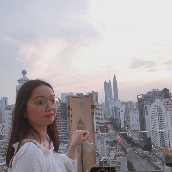 A female student wearing glasses, standing on a balcony overlooking a city skyline