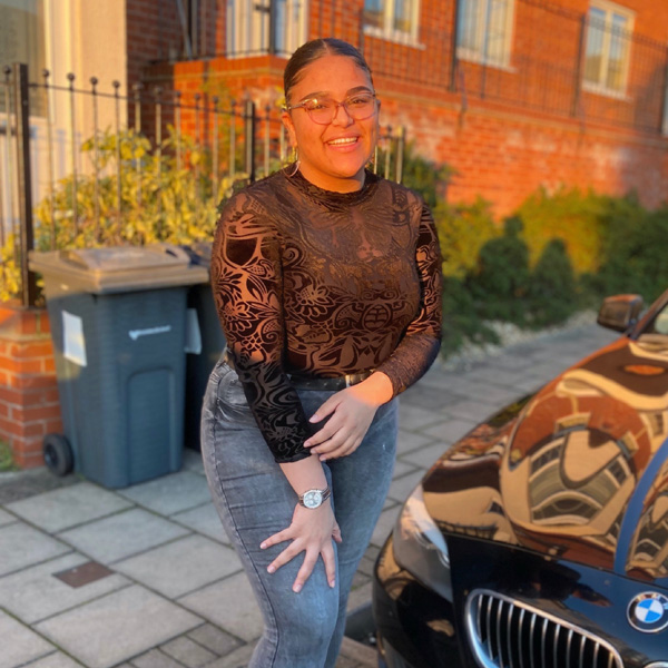 A female student standing in the street next to a car, wearing a black top and jeans