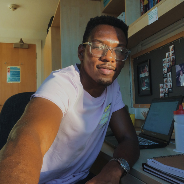 A male student with a camera, sitting at a table looking at the camera