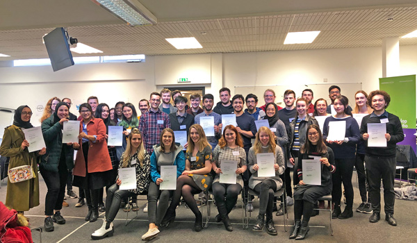 A large group of students in a seminar room holding certificates