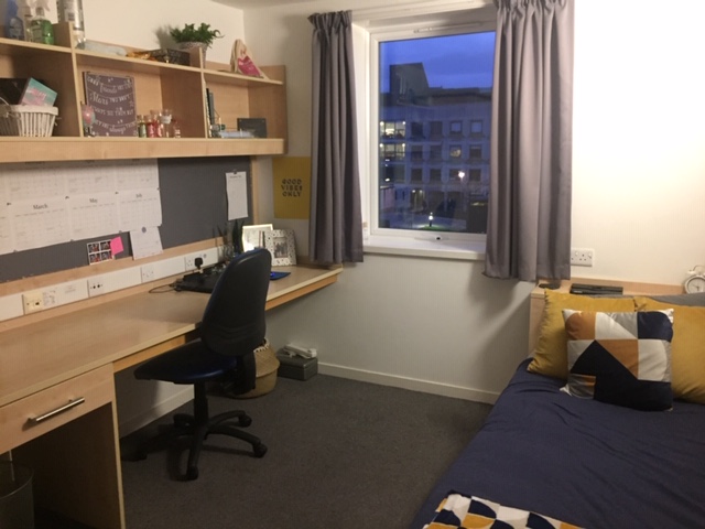 A student bedroom with navy bedcovers and mustard and white cushions