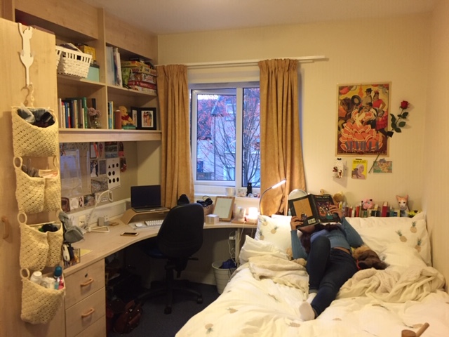 A student bedroom,with a female student lying on the bed, reading