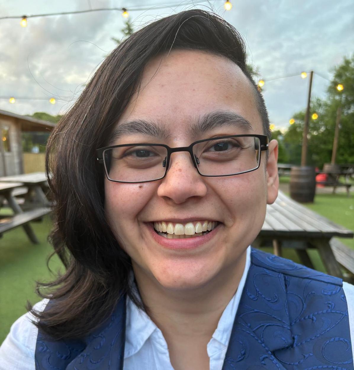 Panellist Sophie Rawnsley-Lau in a beer garden, wearing glasses and a blue waistcoat and shirt.