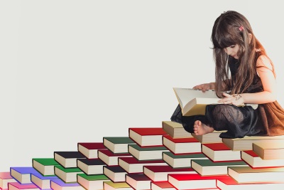 Girl reading a book whilst appearing to sit on a large pile of books
