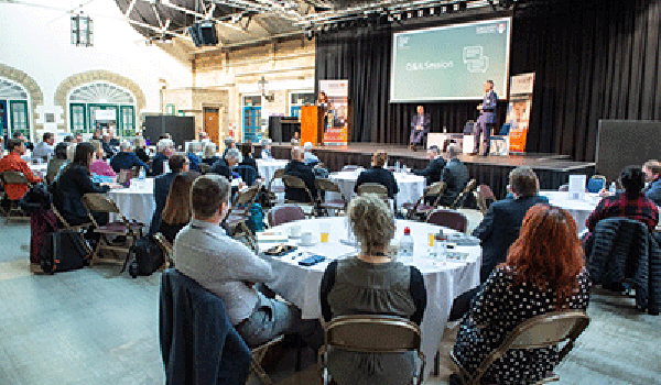 Picture of a conference/events with delegates collaborating at tables. 