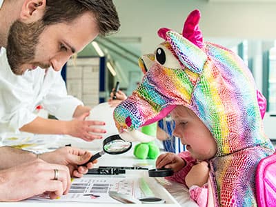A scientist doing research with a girl in a dragon costume looking on 